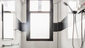 A bathroom with a black and white checkered floor, a white sink, a toilet, and a shower with a handheld showerhead. - Udomsuk Hotel (Satun)