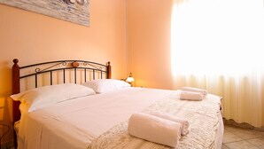 A neatly made bed with white linens, a wooden headboard, and a rolled towel on the bed.