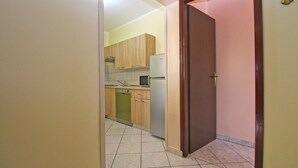 A narrow hallway leading to a kitchen with wooden cabinets, a microwave, and a refrigerator.
