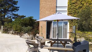 An outdoor patio with wicker chairs, a wooden table, and a large umbrella. - Villa nature beach (Solaro)