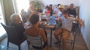A group of people dining at a table with plates of food, a bottle of wine, and a potted plant. - Villa nature beach (Solaro)