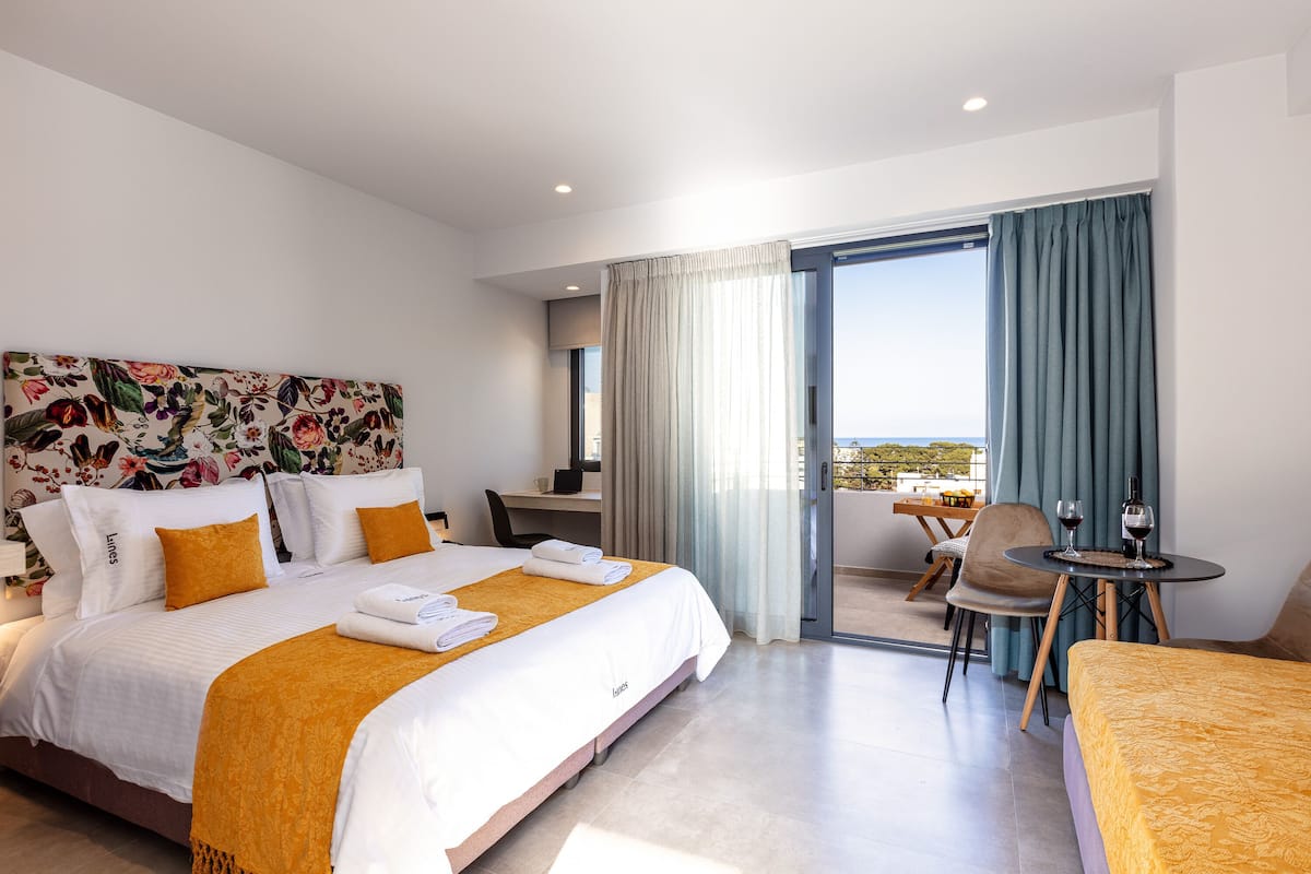 A hotel room with a large bed, a desk, a chair, and a balcony with a table and chairs.