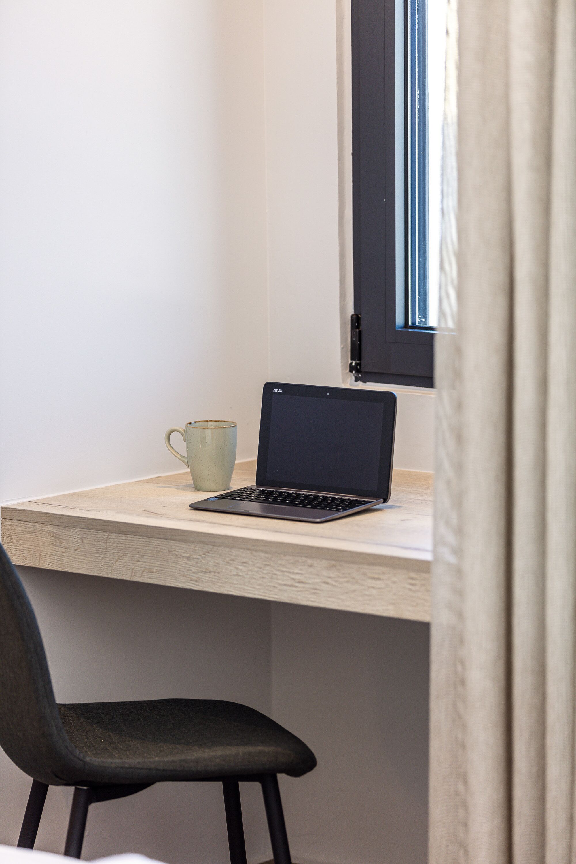 Una computadora portátil sobre un escritorio de madera, con una taza y una silla.