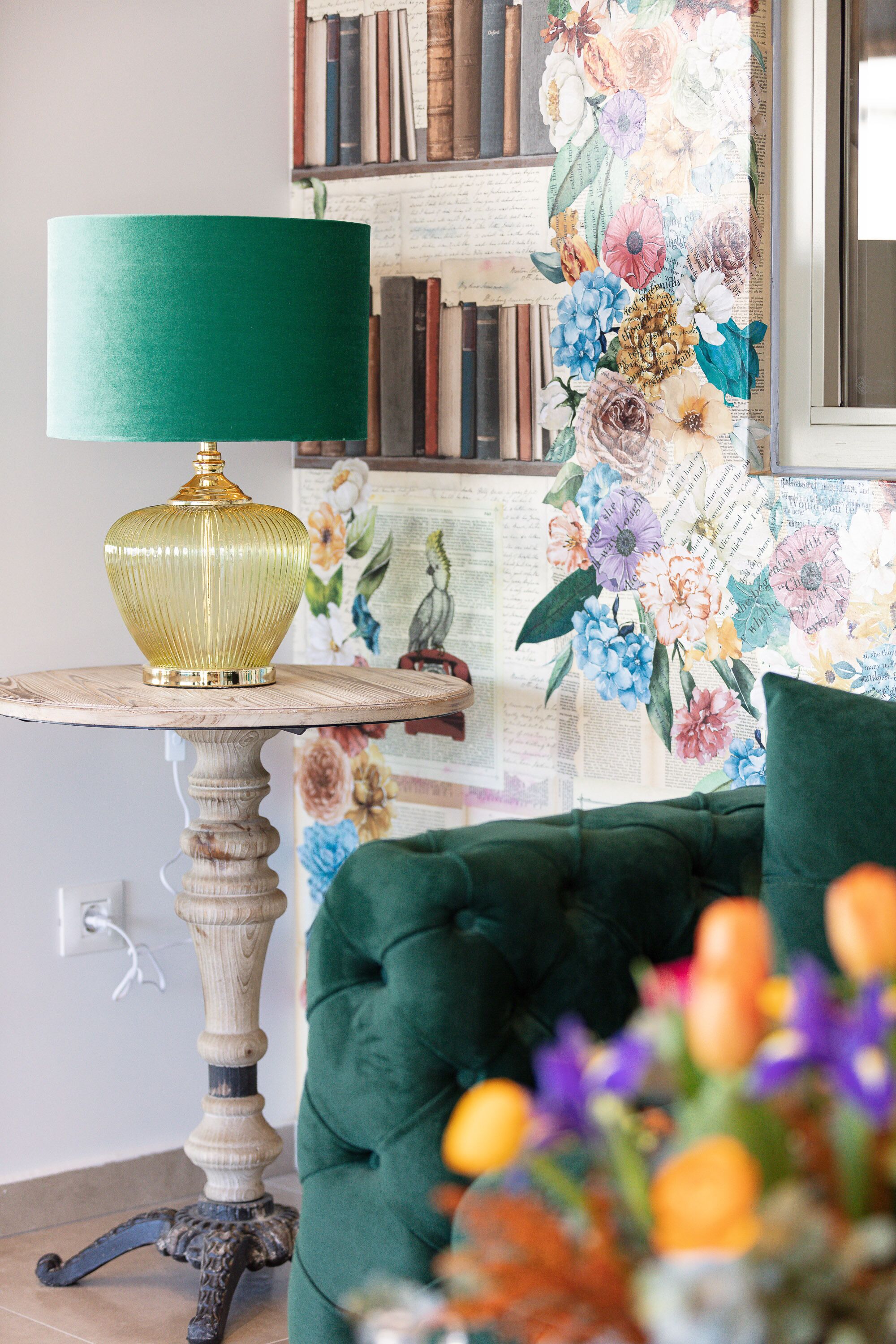Una habitación con una butaca tapizada de verde, una mesa con una lámpara verde y un papel tapiz floral.
