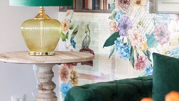 Una habitación con una butaca tapizada de verde, una mesa con una lámpara verde y un papel tapiz floral.