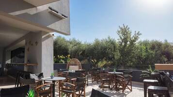 An outdoor patio with multiple wooden tables and chairs, a wicker chair, and potted plants.