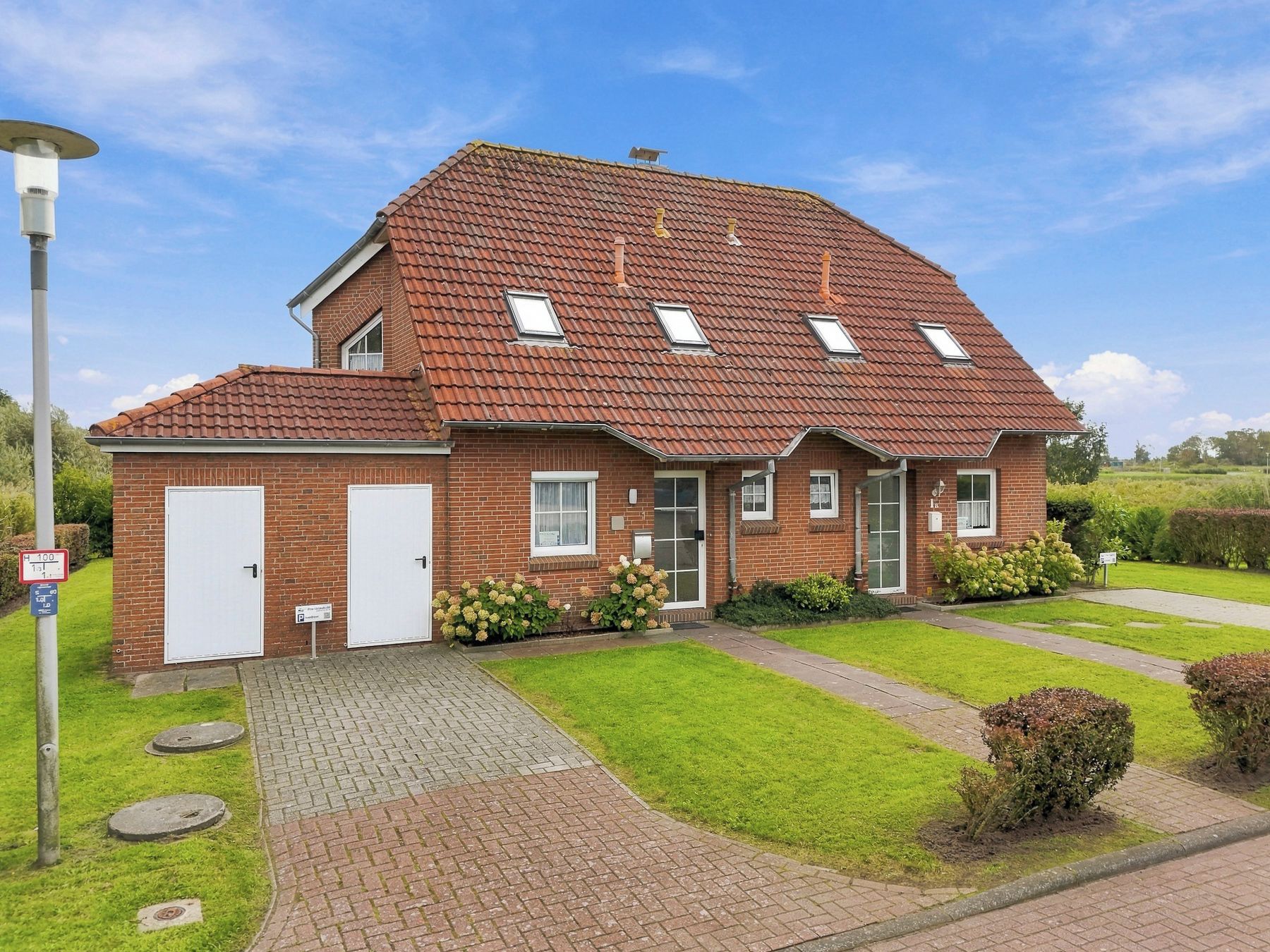 Ein zweistöckiges Backsteinhaus mit rotem Ziegeldach, einer Veranda und einem kleinen Garten.