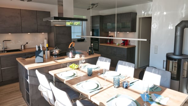 Uma cozinha moderna com ilha central, eletrodomésticos embutidos e área de jantar com uma mesa grande para seis pessoas.