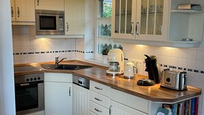 A modern kitchen with white cabinetry, a microwave, an oven, a coffee maker, and a toaster. - Beautiful vacation home in a cul-de-sac location with unobstructed views (Greetsiel)