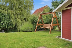 Un ensemble de balançoires en bois dans un jardin, avec un bâtiment rouge en arrière-plan.
