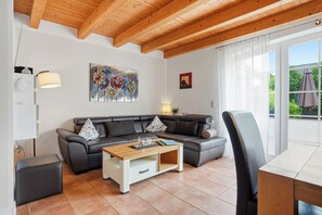 Un salon comprenant un canapé d’angle, une table basse, un téléviseur et une fenêtre avec des rideaux.