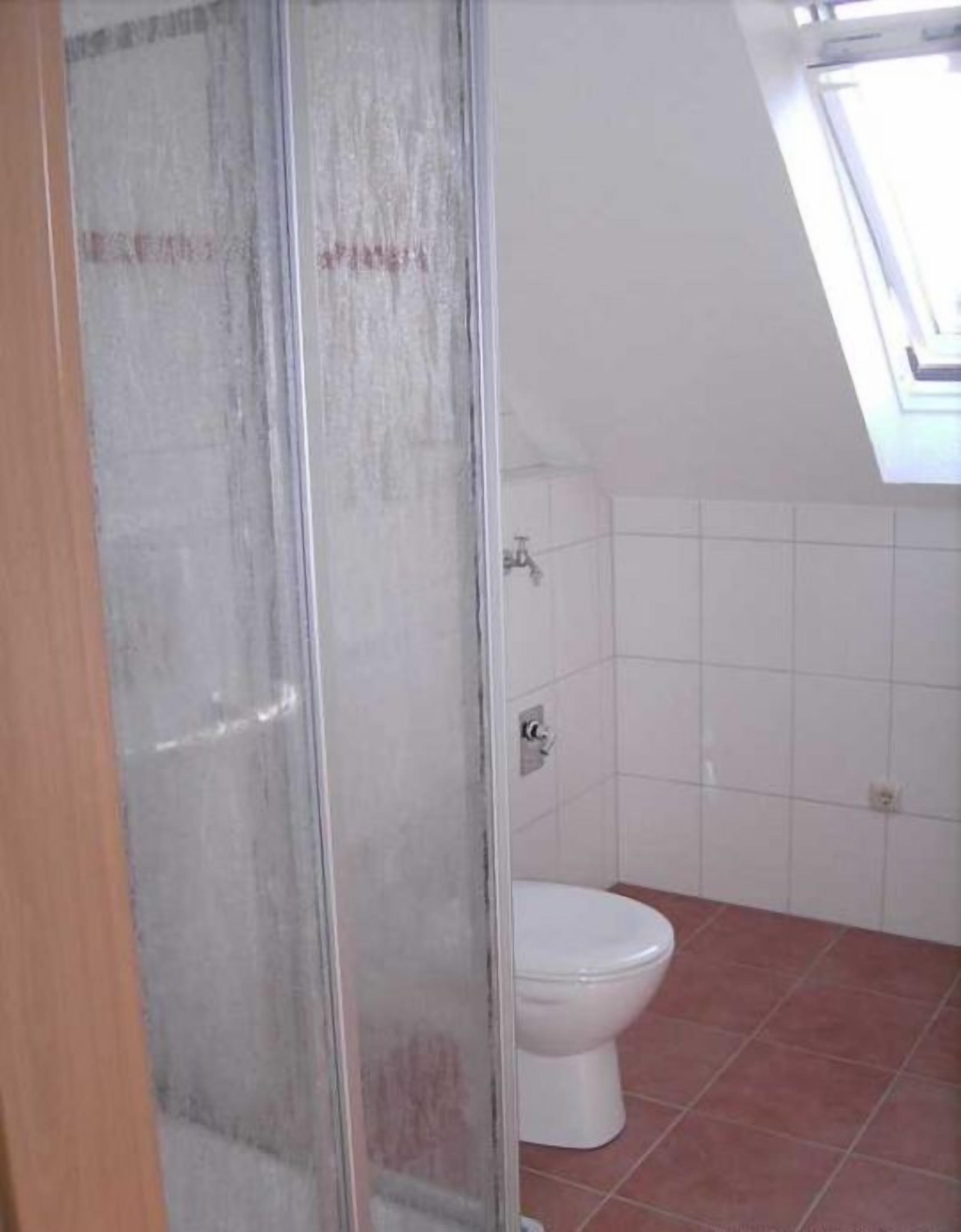 Un baño con cabina de ducha, inodoro y suelo de baldosas.