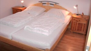 Een tweepersoonsbed met houten hoofdeinde en voeteinde, twee nachtkastjes met lampen, en een houten vloer.