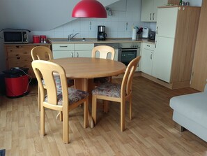 A compact kitchen with a dining table, chairs, and a red overhead light. - Schöne Ferienwohnung in Deichnähe (Norddeich)