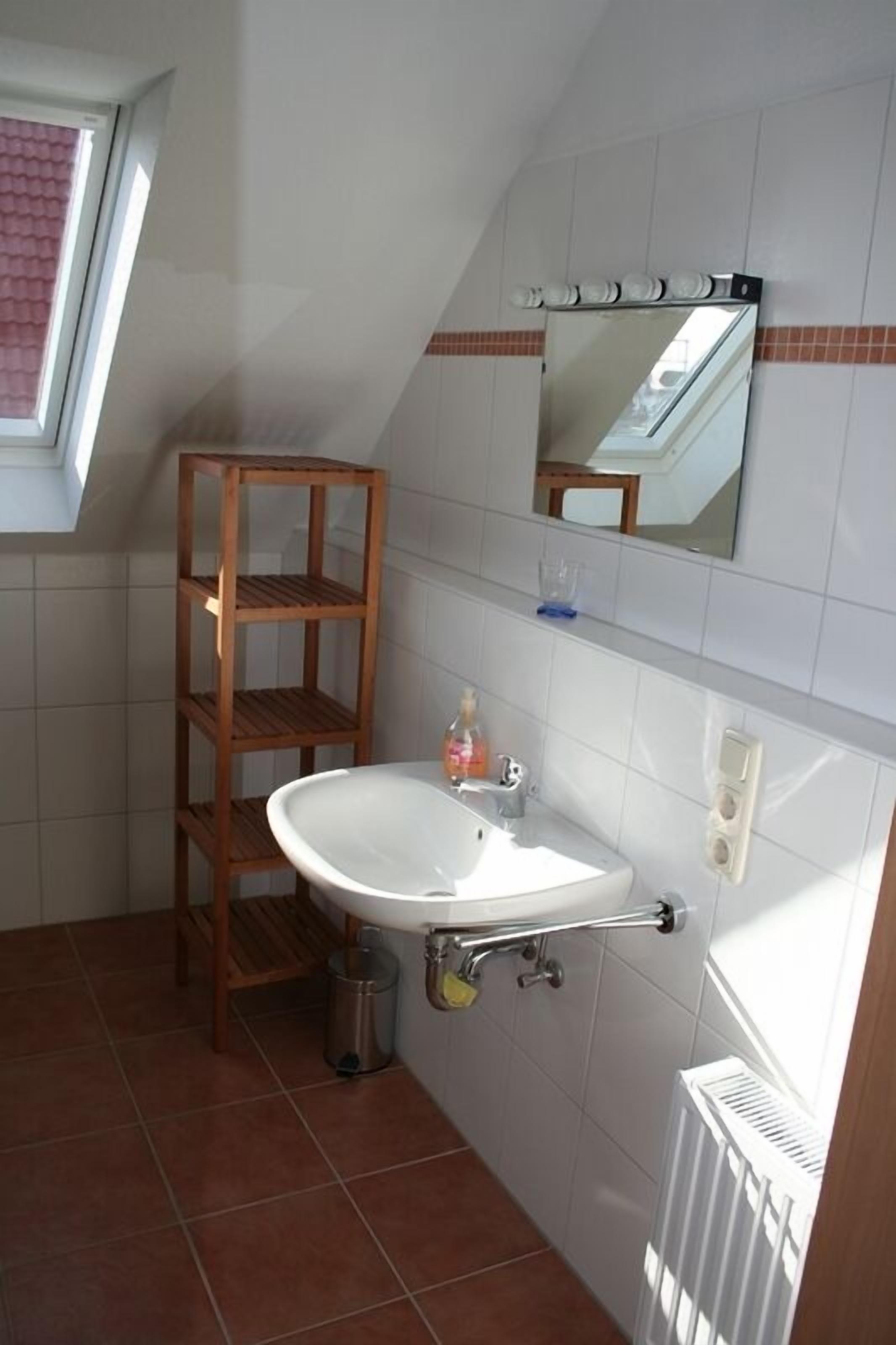 A bathroom with a white sink, a wooden shelf, a mirror, and a window.