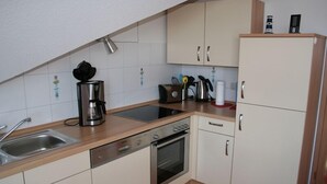 Een compacte keuken met een vaatwasser, oven, koffiezetapparaat en een kleine koelkast.