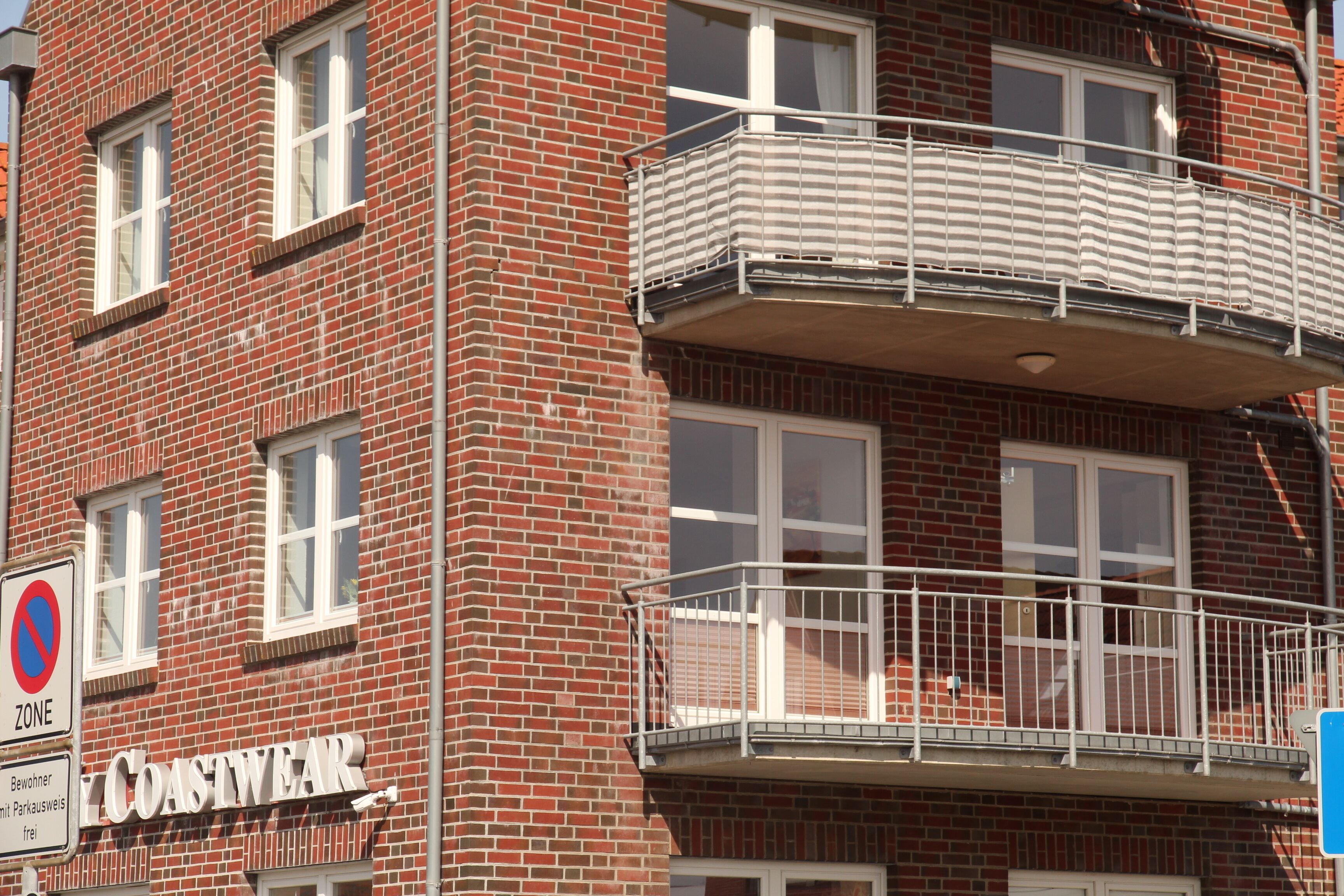A multi-story brick building with a no parking zone sign, a store named 'COASTWEAR,' and a balcony with a metal railing.