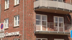 Ein mehrstöckiges Backsteingebäude mit einem Verbotsschild für Parkplätze, einem Geschäft namens 'COASTWEAR' und einem Balkon mit einem Metallgeländer.