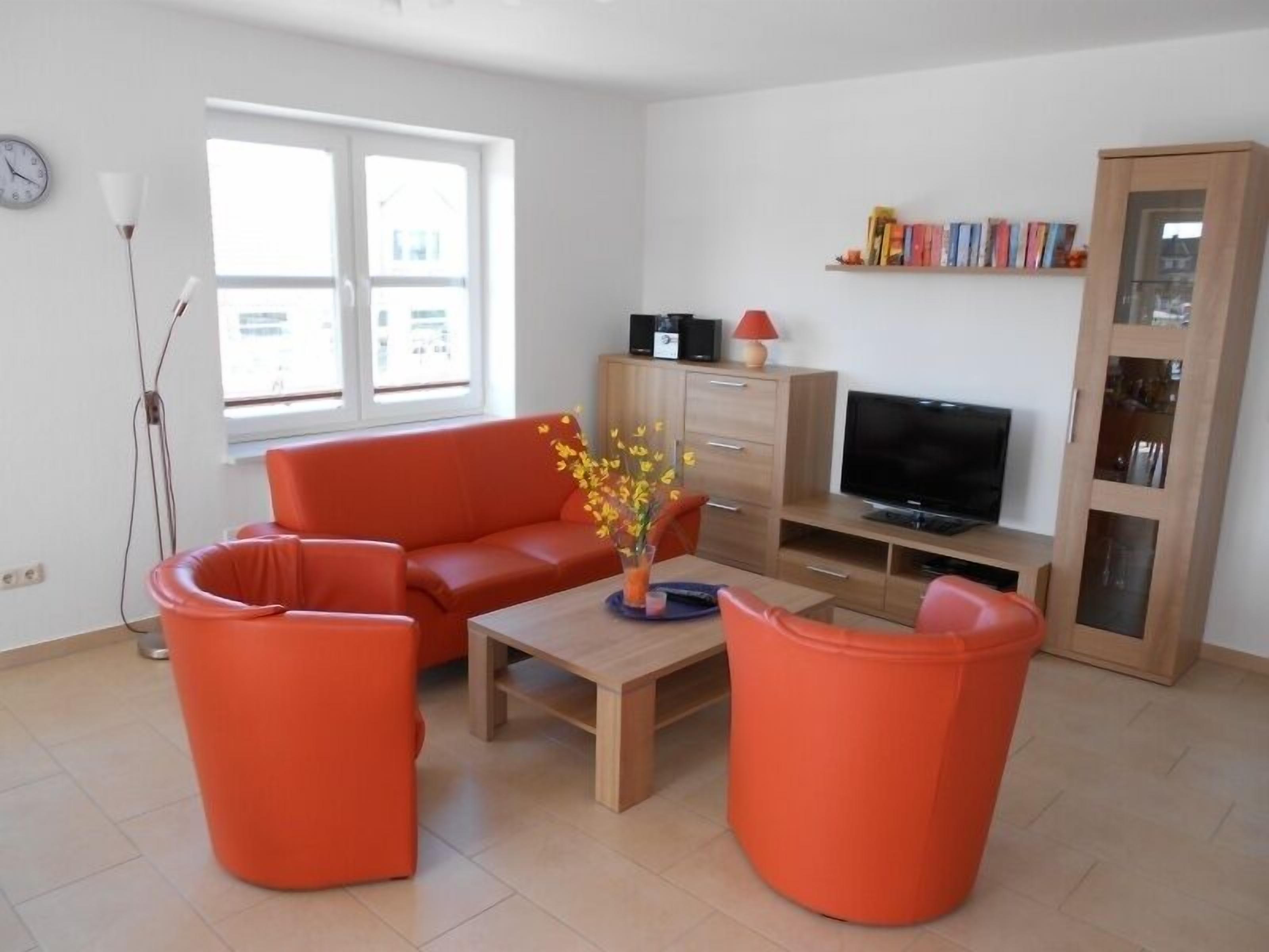 Ein modernes Wohnzimmer mit einer Couch, zwei Sesseln, einem Couchtisch, einem Fernseher und einem Bücherregal.