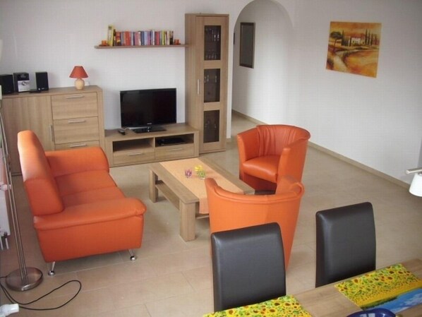 Un salon avec des canapés orange, un téléviseur, une bibliothèque et un tableau accroché au mur.