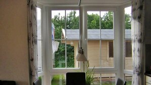Zona pranzo con tavolo e sedie, un lampadario e vista su una casa e del verde all'esterno.