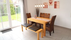 Uma área de refeições com mesa de madeira, quatro cadeiras de vime e dois bancos.