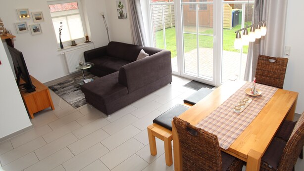 Uma sala de estar moderna com sofá, uma mesa de jantar com cadeiras e uma grande porta de vidro deslizante que dá para um quintal.