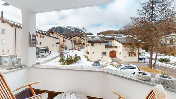 Uma varanda com vista para uma rua coberta de neve, edifícios e montanhas.
