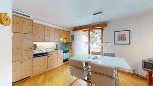 Cozinha moderna com armários de madeira, bancada de granito e área de refeições com mesa e cadeiras de vidro.