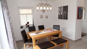 A dining area with a wooden table, black chairs, and a bench. There are wall art pieces and a window with blinds. - Gemütliches Ferienhaus in Greetsiel (Greetsiel)