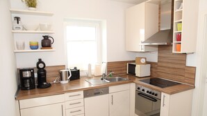 A modern kitchen with white cabinets, a wooden countertop, a built-in oven, and a coffee maker. - Gemütliches Ferienhaus in Greetsiel (Greetsiel)