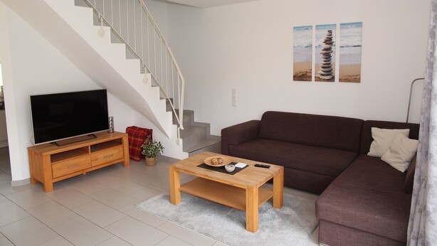 A living room with a TV, wooden coffee table, brown sofa, and a staircase. - Gemütliches Ferienhaus in Greetsiel (Greetsiel)