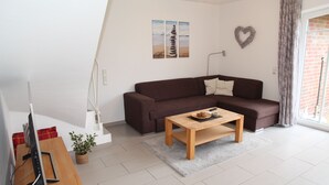A modern living room with a brown sofa, a wooden coffee table, a TV on a stand, and a potted plant. - Gemütliches Ferienhaus in Greetsiel (Greetsiel)