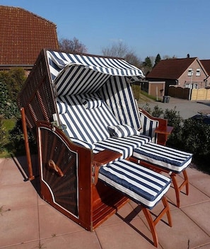 Ein Holz-Loungesessel mit gestreifter Sitzkissen und Netzlehne, platziert auf einer Terrasse mit Blick auf Wohnhäuser.