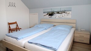Quarto com cama, mesa de cabeceira, cadeira e arte de parede com tema praiano.