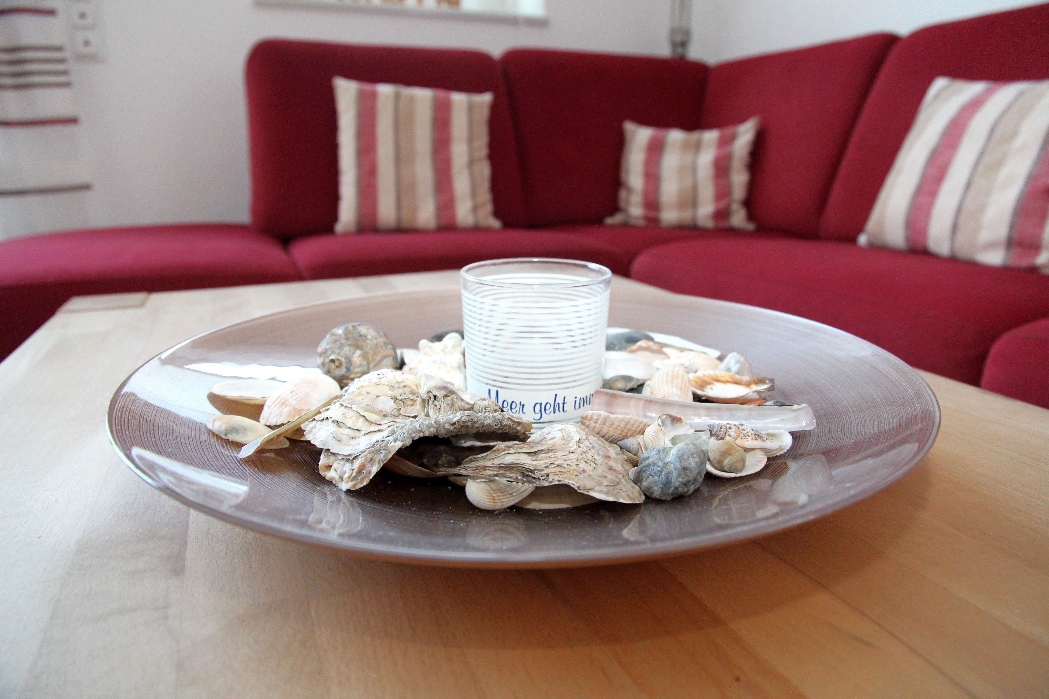 Een bord met schelpen en een glas op een houten tafel in een kamer met een rode bank.