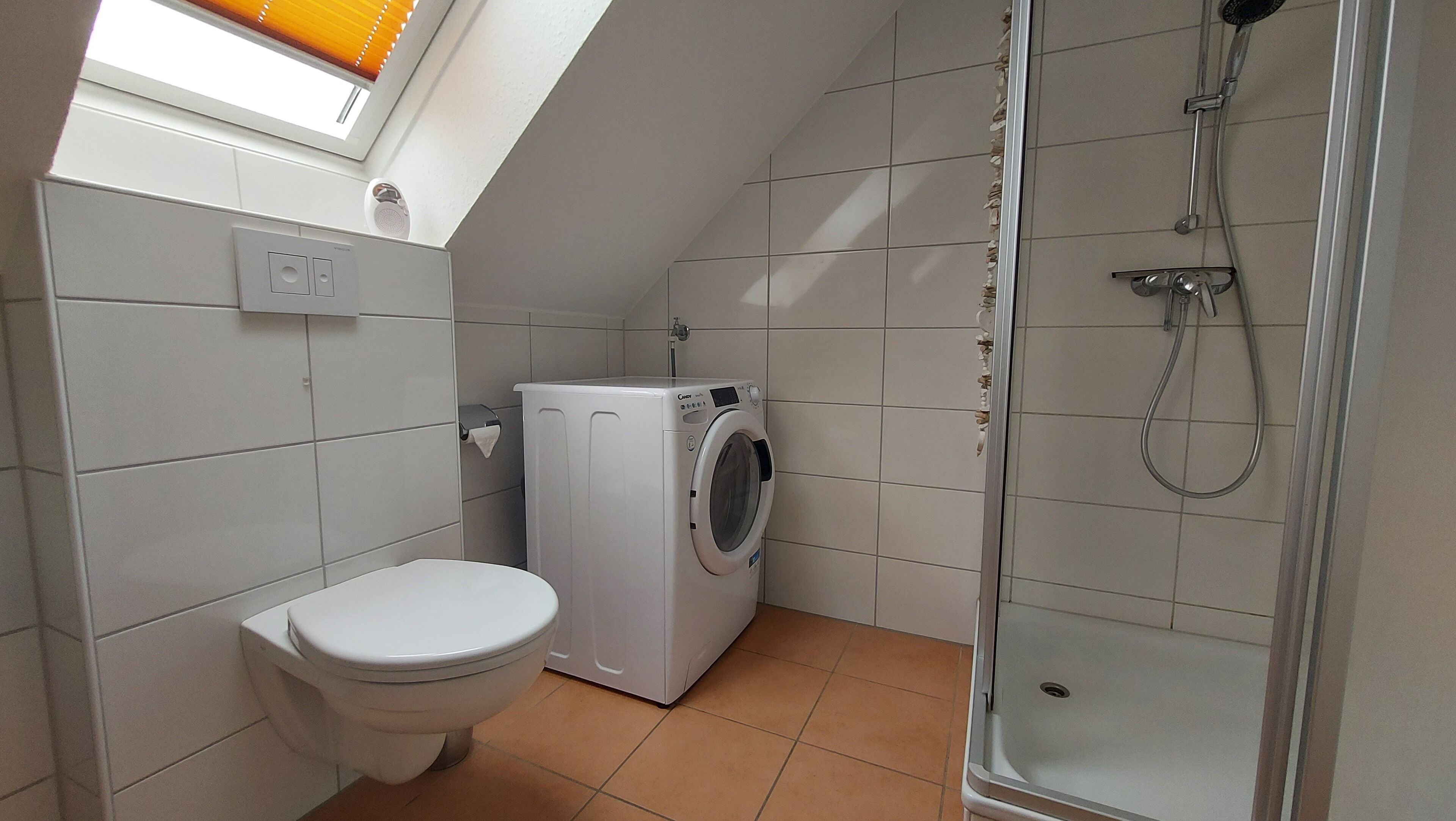 A small, modern bathroom with a toilet, washing machine, and shower.