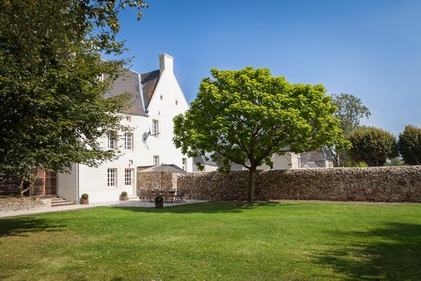 A white building with a stone wall, a tree, and a well-maintained lawn.