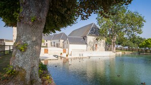 Un bâtiment historique avec un étang, entouré d’arbres et d’un mur de pierre.
