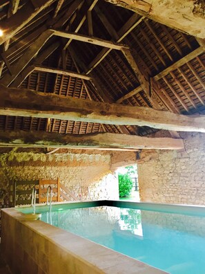An indoor swimming pool with a rustic wooden ceiling and stone walls.