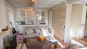 Un salon chaleureux avec une cheminée, un canapé, une table basse sur laquelle sont disposés des fruits, et des œuvres d’art encadrées accrochées au mur.