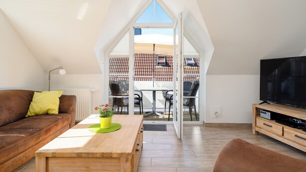 Ein gemütliches Wohnzimmer mit einem braunen Ledersofa, einem Holztisch mit einer grünen Vase und einem Fernseher auf einem Holzständer.