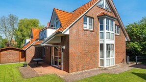 Ein zweistöckiges Backsteinhhaus mit geneigtem Dach, großen Fenstern und einer kleinen Terrasse.