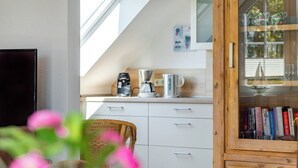 Eine Küche mit weißen Schränken, einer Kaffeemaschine und einem Korbstuhl.