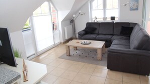 En moderne stue med en grå sofa, et træbord og et stort vindue med persienner.