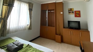 A hotel room with a bed, a wardrobe, a television, and a window with curtains. - KARSA UTAMA HOTEL (Jakarta)