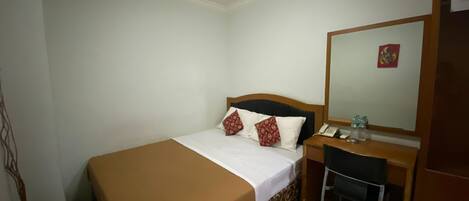 A hotel room with a bed, a desk, a chair, a mirror, and a telephone.