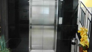 A modern elevator with a metallic finish, flanked by black walls and a white tiled floor. - KARSA UTAMA HOTEL (Jakarta)