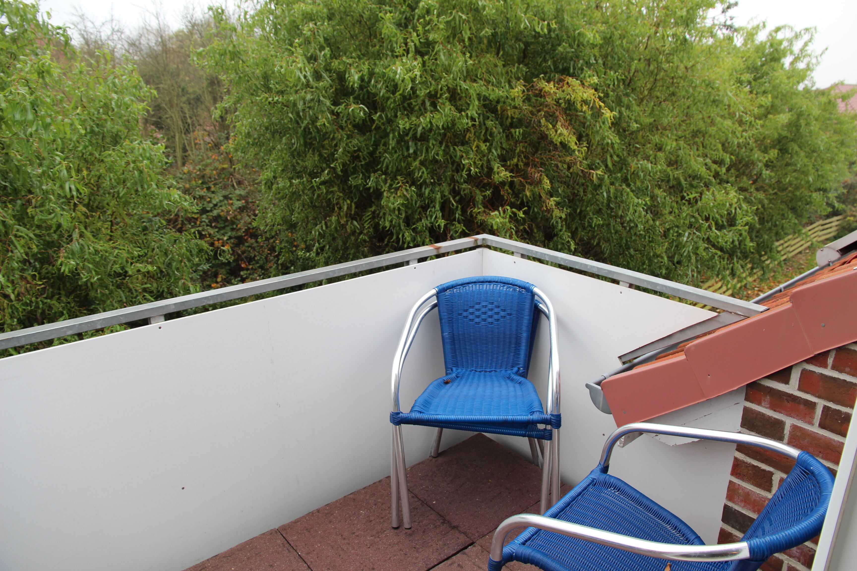 A balcony with two blue chairs and a white railing.