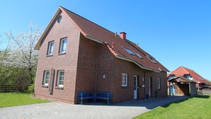 Een bakstenen huis met schuin dak, een veranda en een kleine tuin.